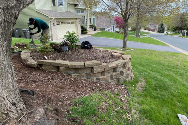 TJB Landscaping professional repairing a modular retaining wall in a residential yard in Minnesota, reinforcing blocks for improved stability and durability.
